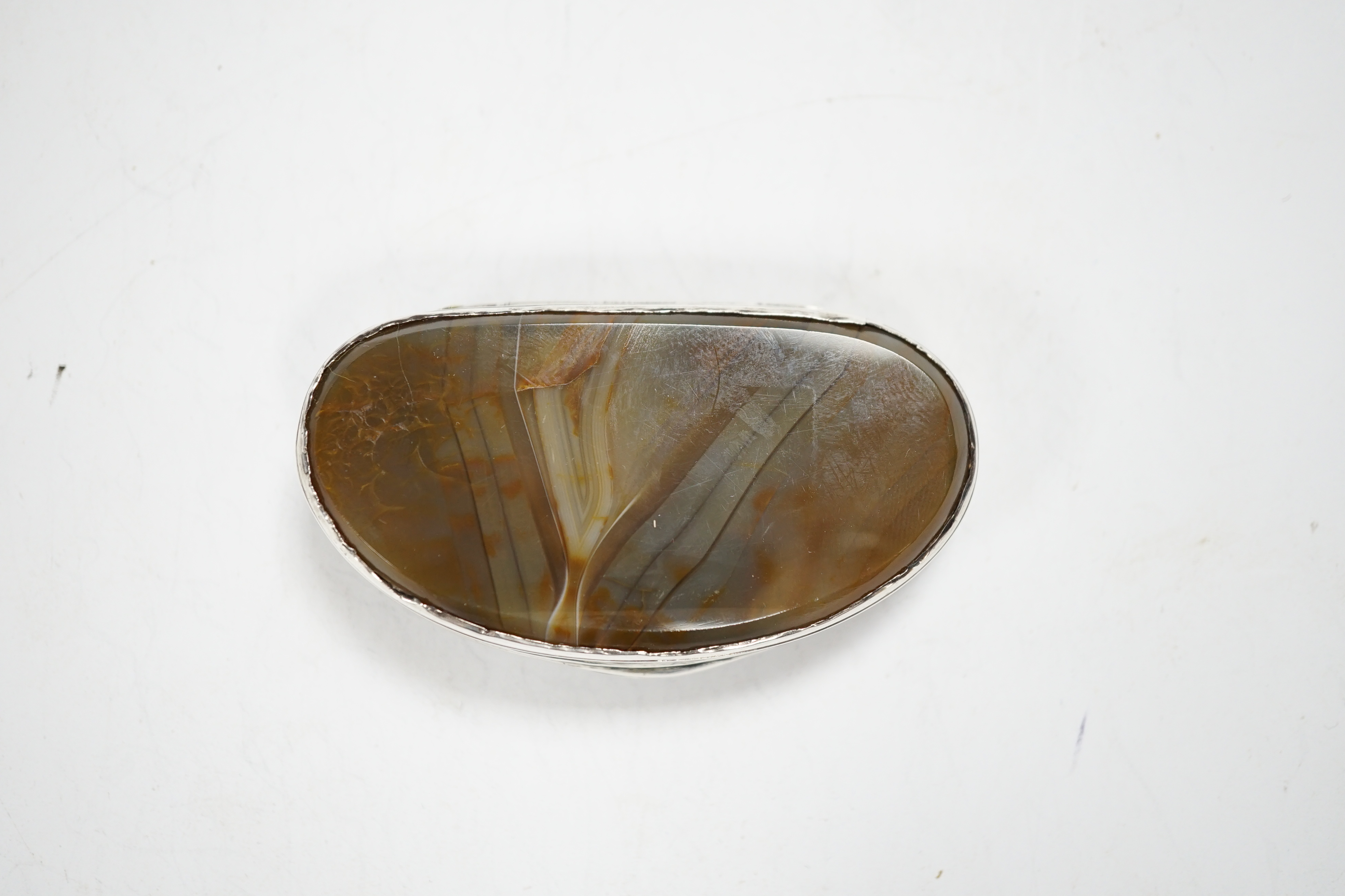 An early 19th century Scottish? white metal oval snuff box, with banded agate base and inset agate lid, decorated with dogs and scrolls, 69mm.